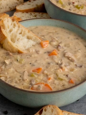 A piece of bread in a bowl of chicken wild rice soup.