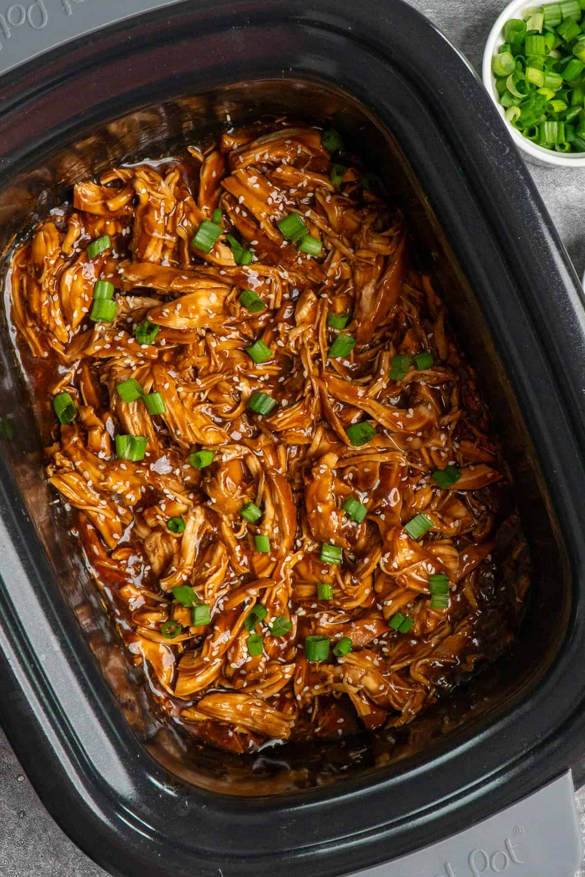Overhead look at crock pot teriyaki chicken garnished with green onions and sesame seeds.