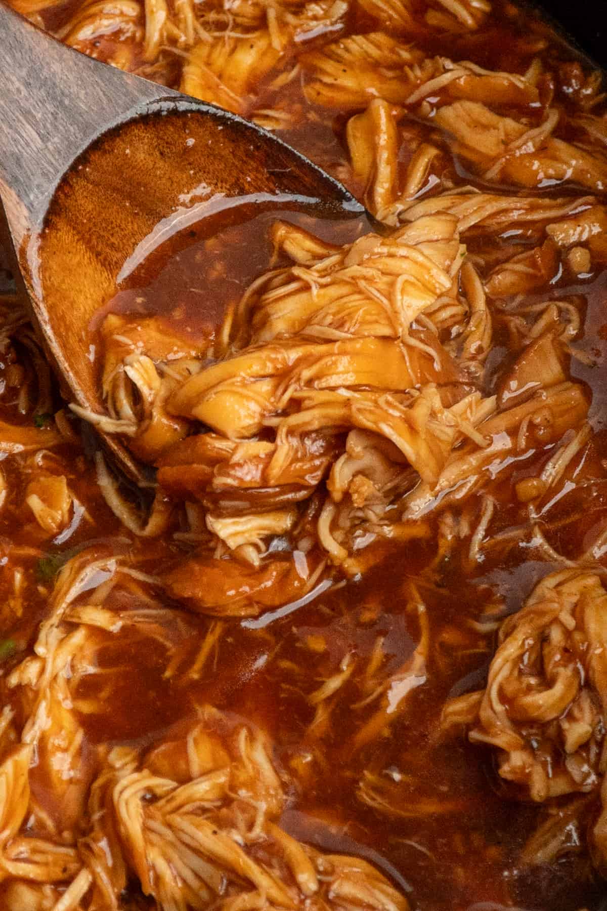 Close-up of a wooden spoon in root beer chicken in a crock pot