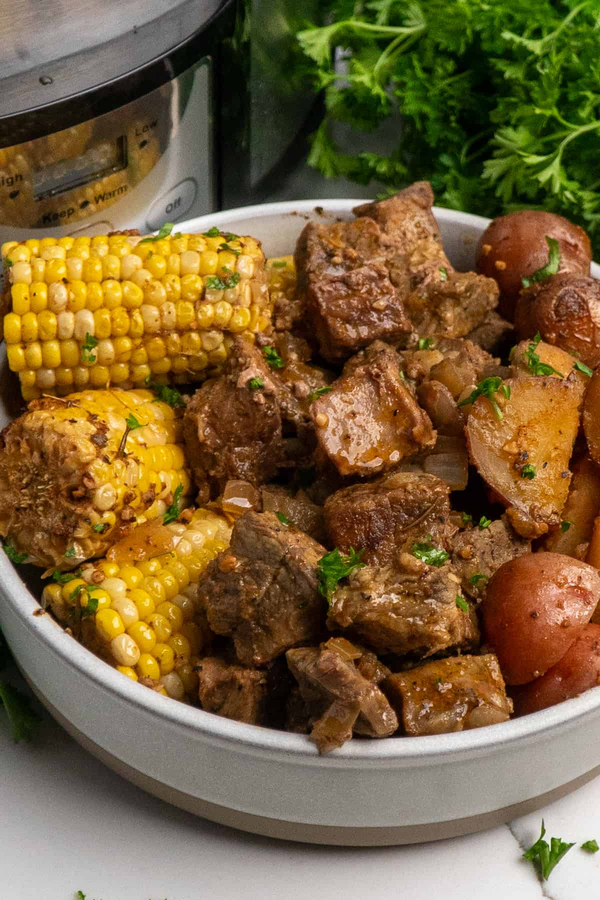 A bowl full of steak bites, corn on the cob and red potatoes.