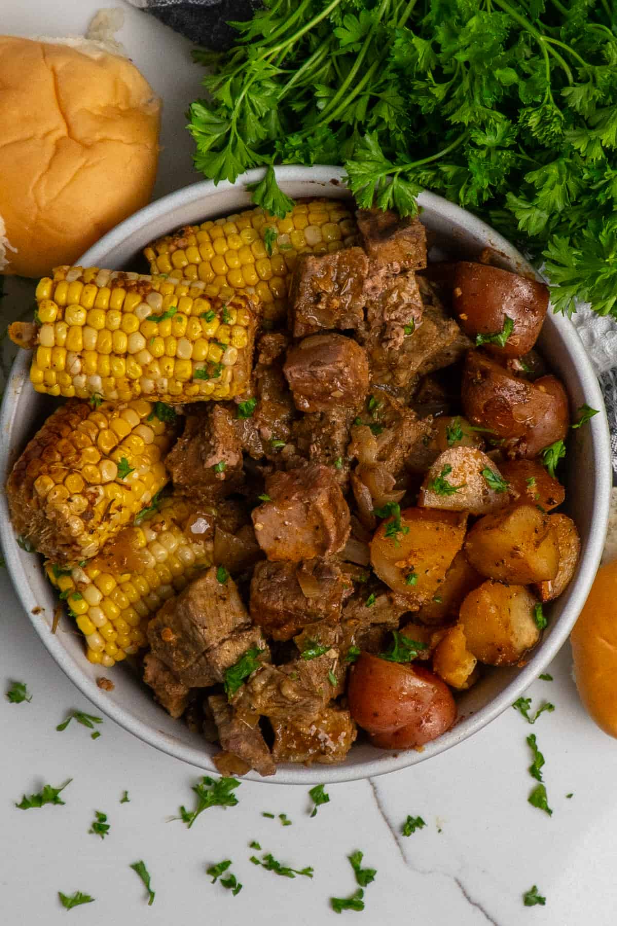 Overhead look at a bowl full of steak bites, corn on the cob and red potatoes.