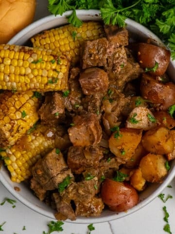 Overhead look at a bowl full of steak bites, corn on the cob and red potatoes.