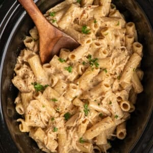 A wooden spoon in crock pot garlic parmesan chicken pasta.
