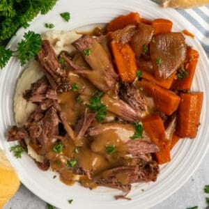 Overhead look at a 3 packet pot roast on a plate of mashed potatoes.