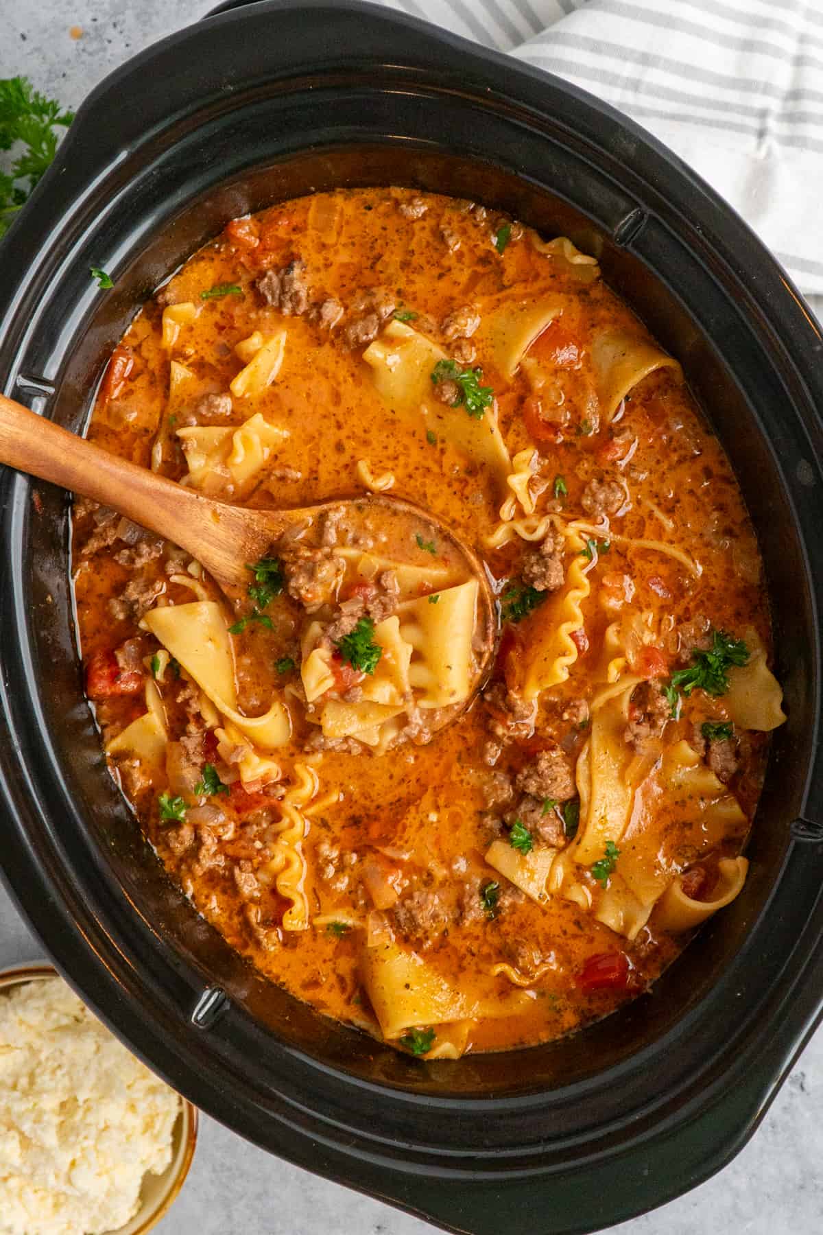 A wooden ladle of lasagna soup in a slow cooker.