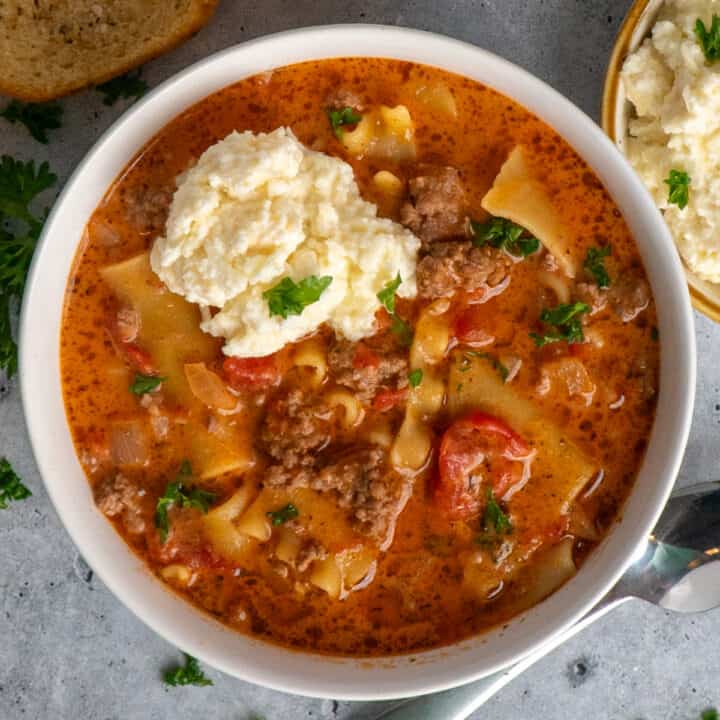 A bowl full of lasagna soup topped with ricotta cheese.