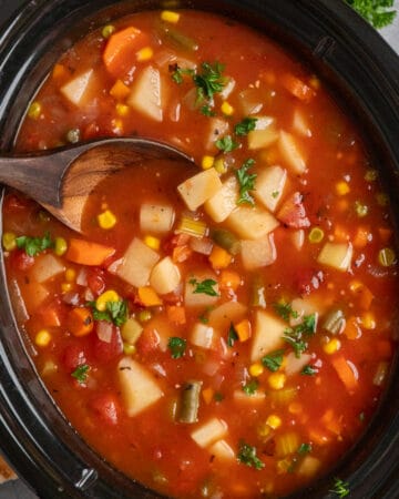 Overhead look at a wooden spoon in crock pot vegetable soup.