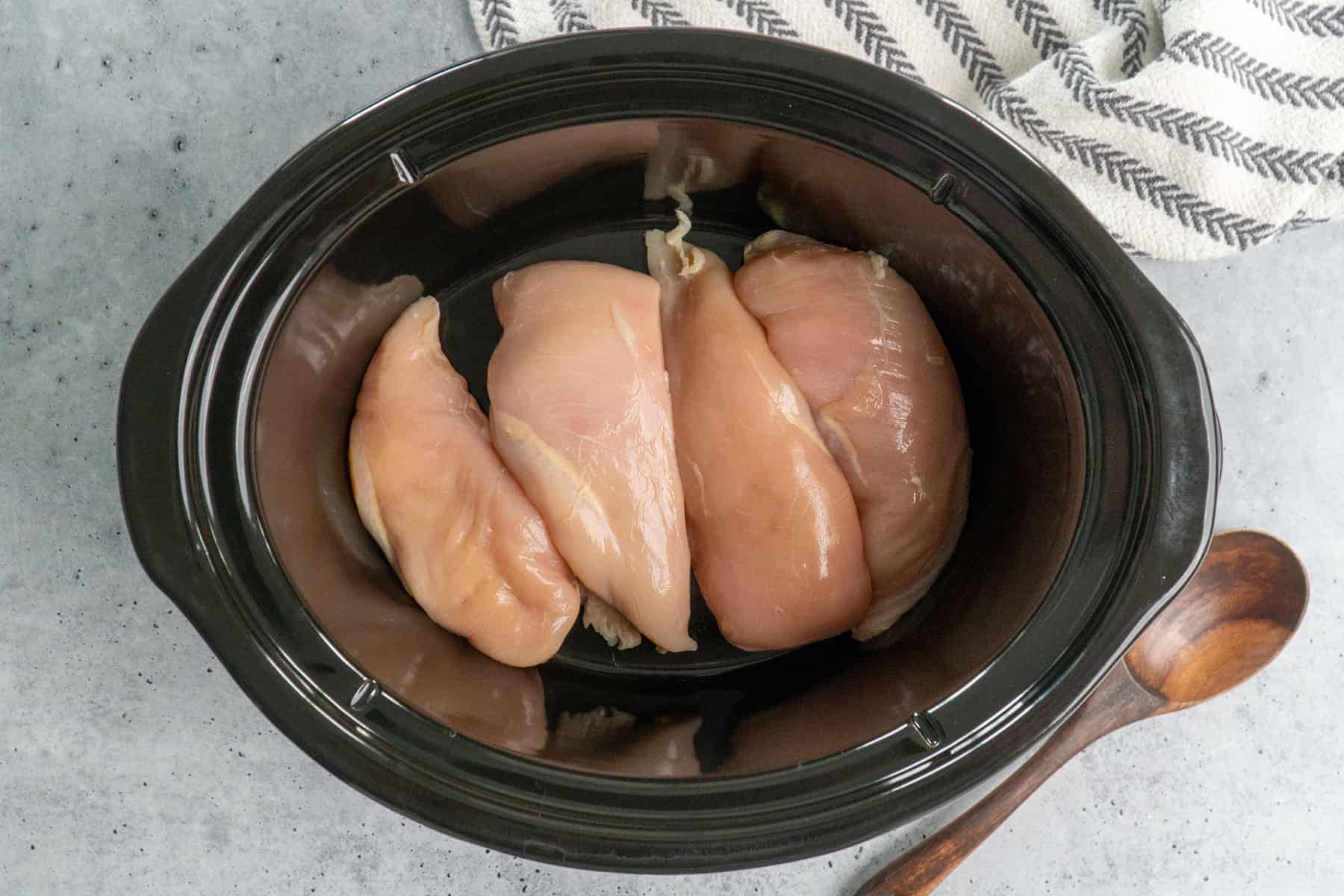 Four chicken breasts in a slow cooker.
