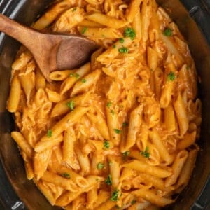 Close up of pink sauce pasta in a slow cooker with a wooden spoon.