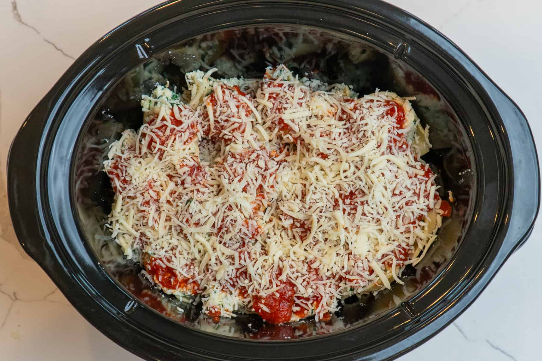Stuffed shells in a slow cooker topped with cheese and ready to be cooked.