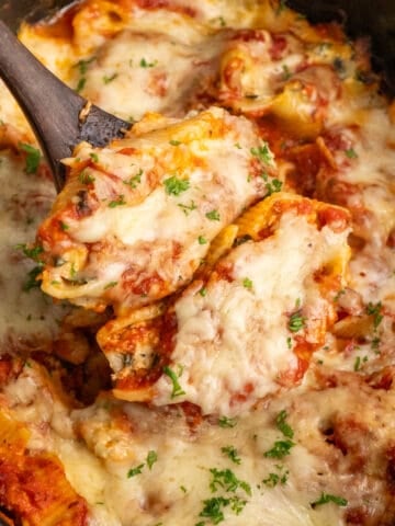 Close up of a wooden spoon holding two crockpot stuffed shells.