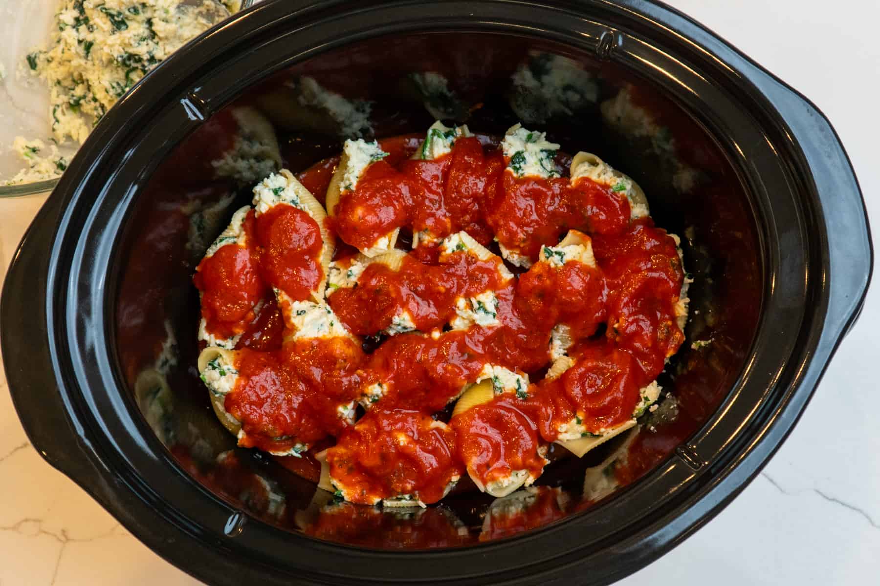 Stuffed shells in a slow cooker topped with marinara sauce.