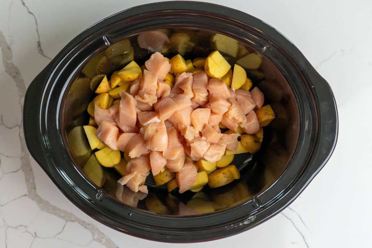 Cubed chicken and potatoes in a slow cooker.