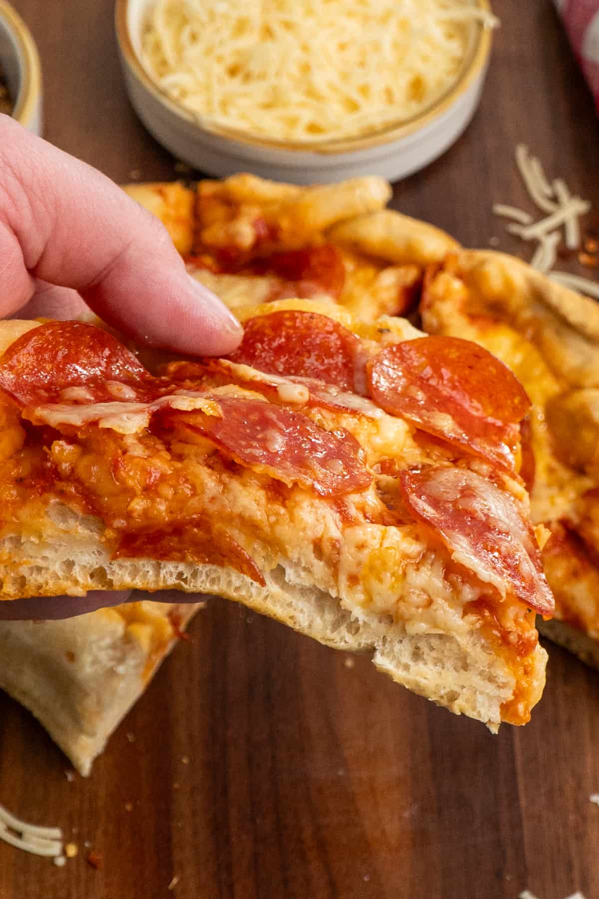 A hand holding a piece of thick crust pepperoni pizza.