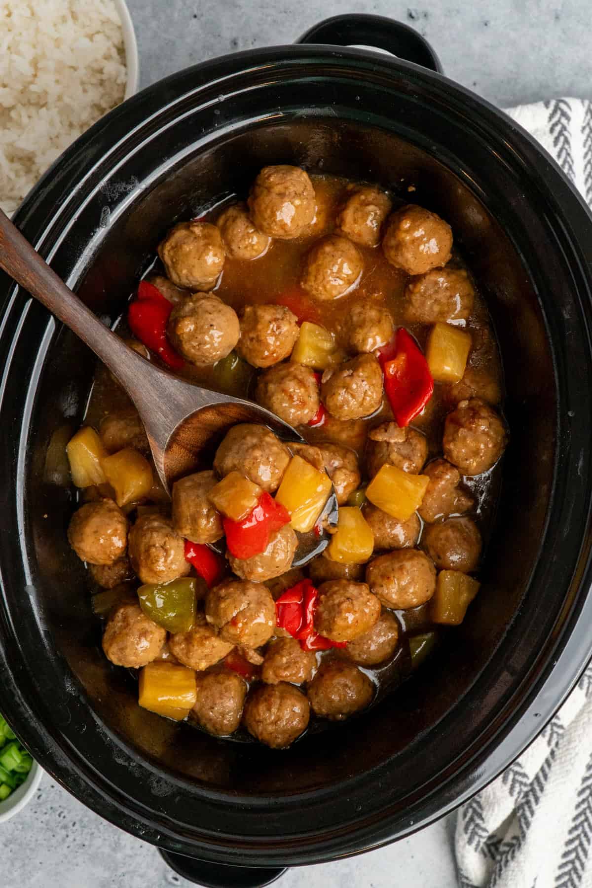 Overhead look at teriyaki meatballs in a crock pot with a wooden spoon.