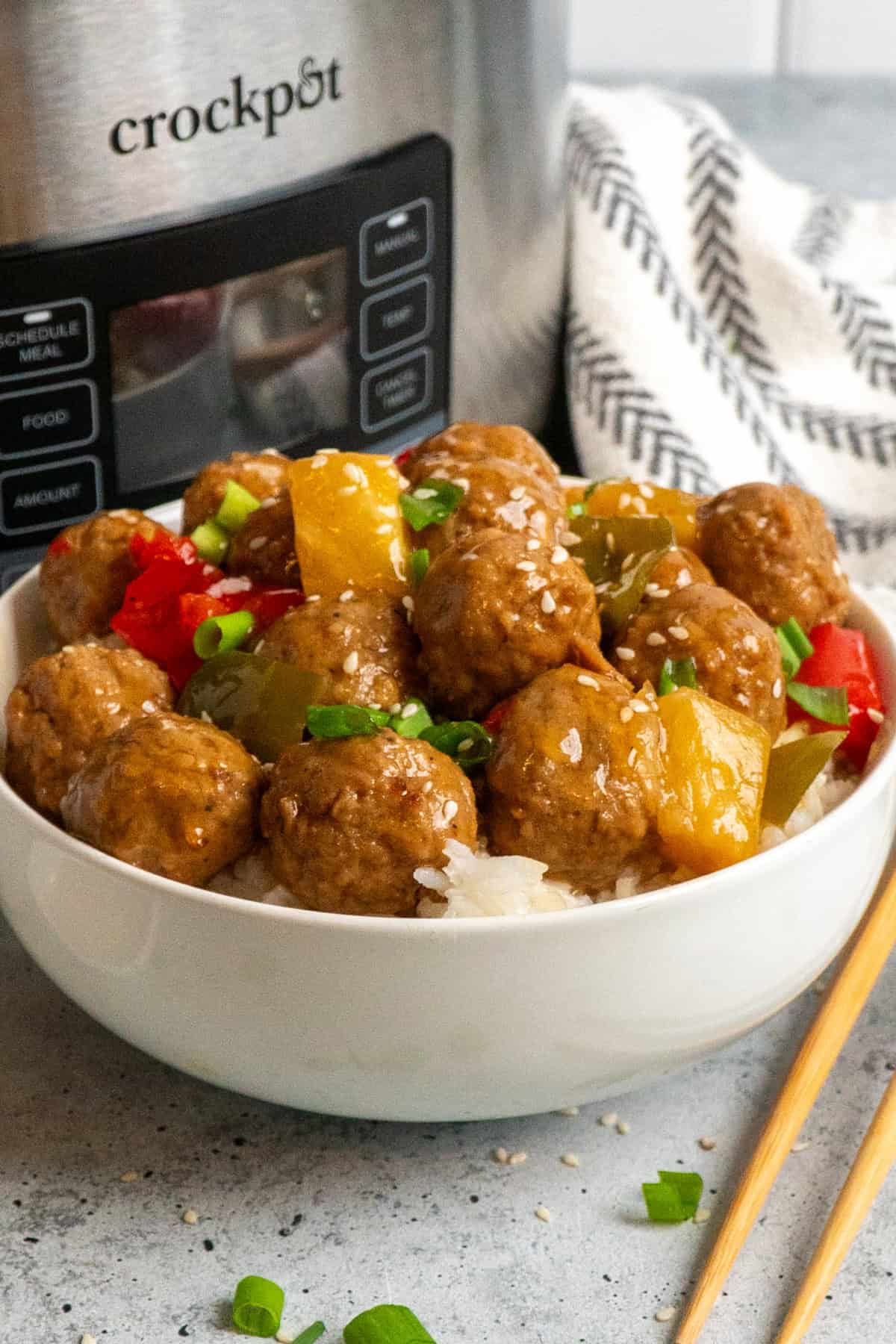 Close up of teriyaki meatballs over a white bowl of rice with a crock pot in the background.