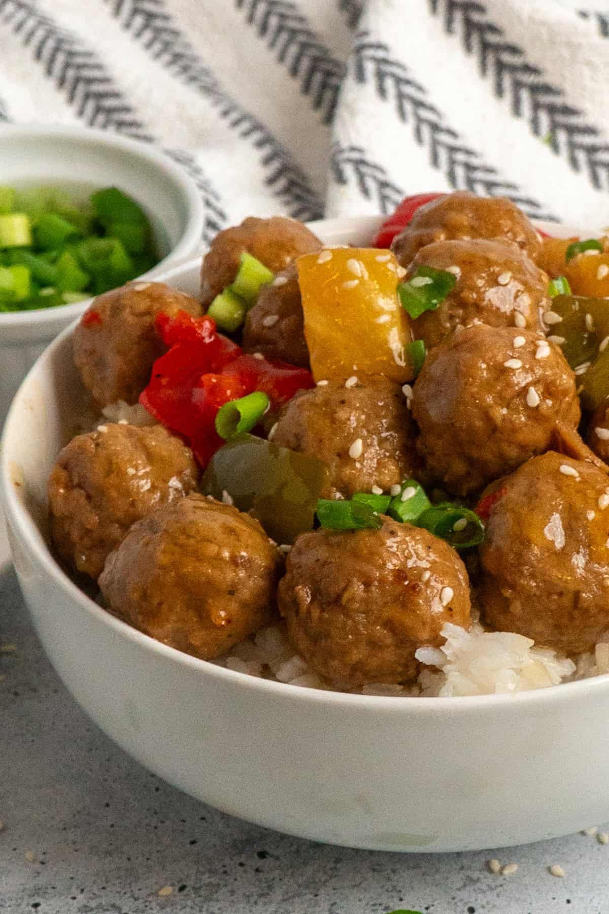 Close up of teriyaki meatballs over a white bowl of rice.