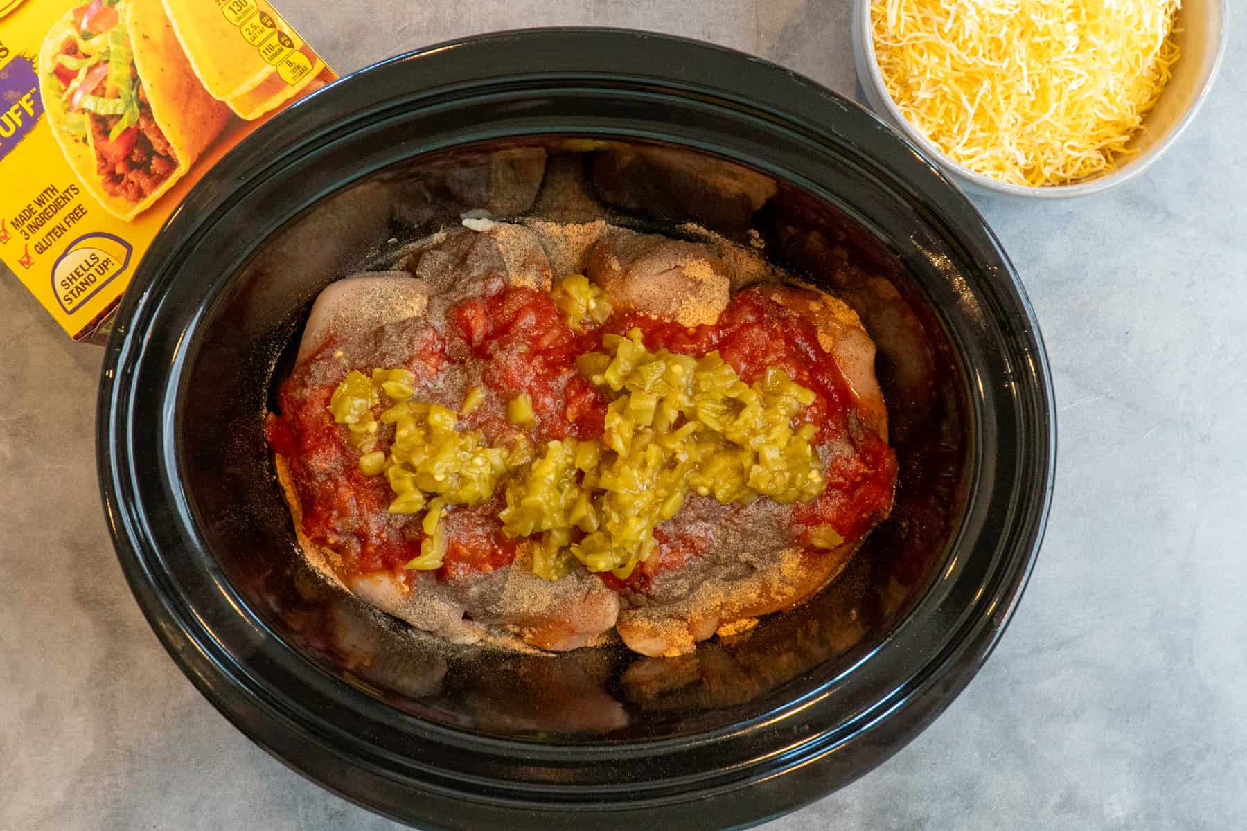 Overhead look at chicken, spices, salsa, and green chilies in a crock pot.