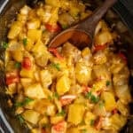 Overhead look at Crock Pot breakfast potatoes with a wooden spoon in them.