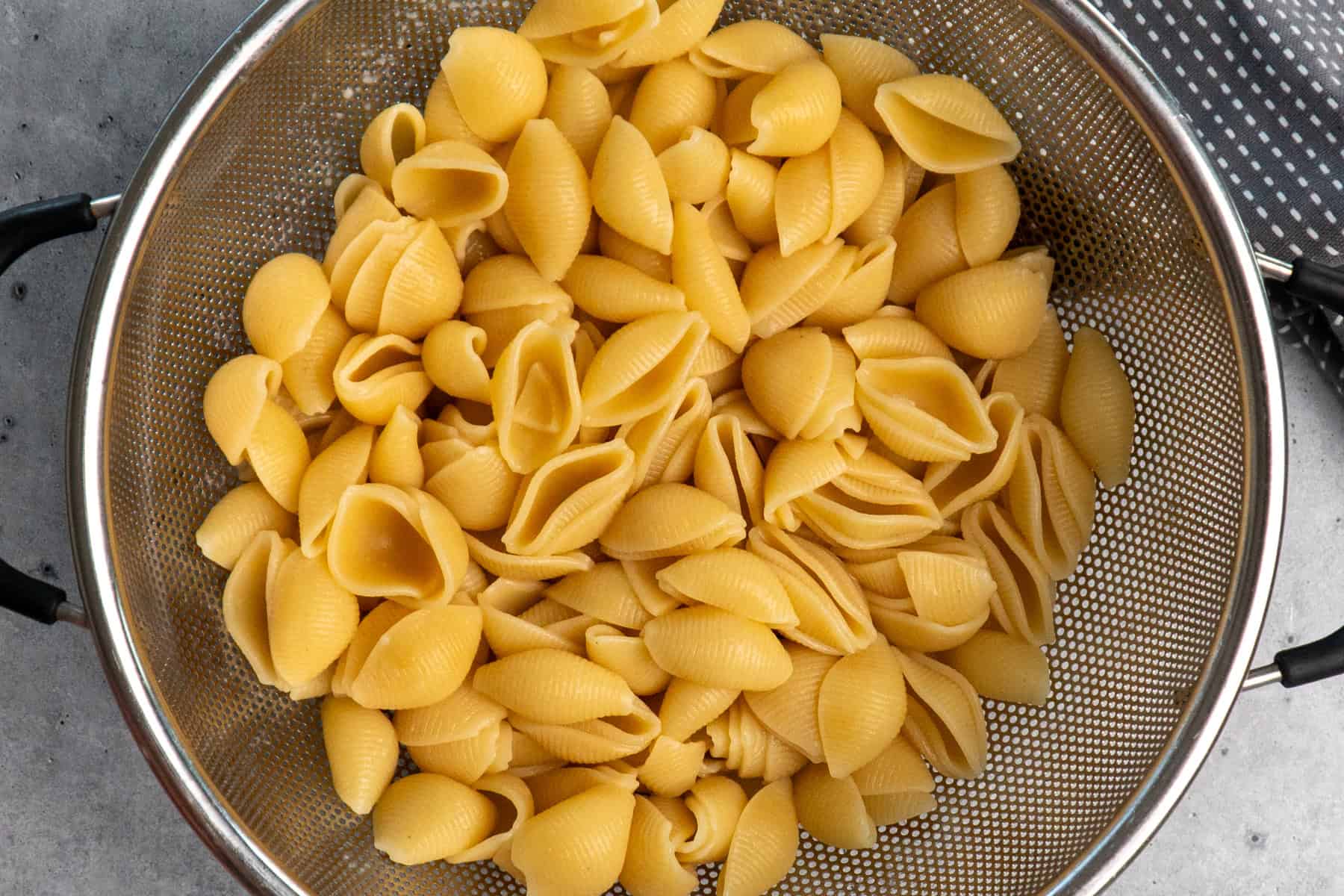 Cooked macaroni shells in a strainer.