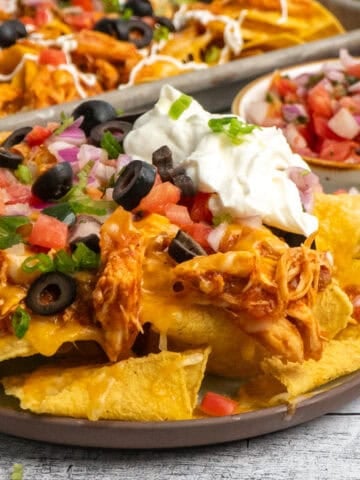 Close up of slow cooker chicken nachos on a plate with lots of toppings.