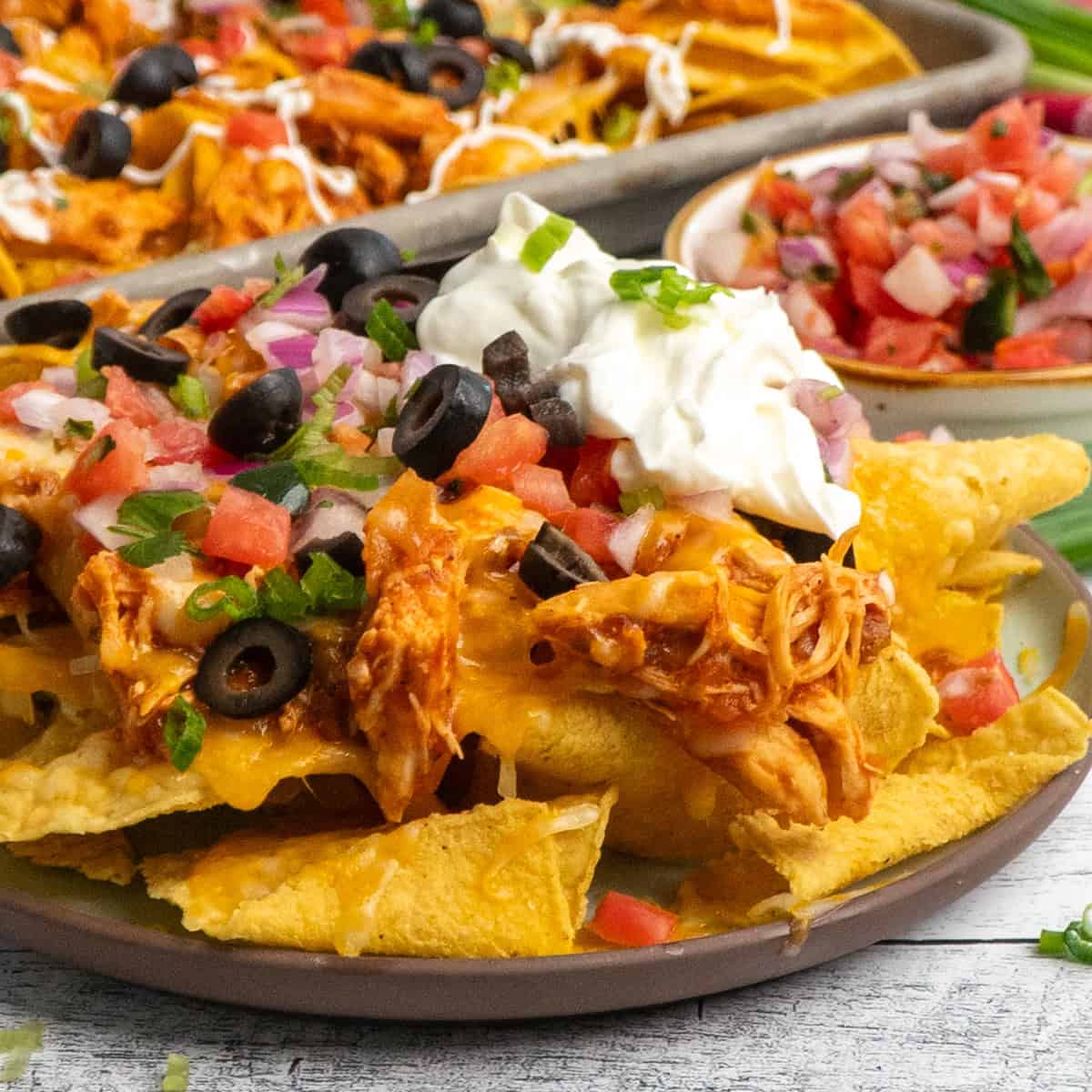 Close up of slow cooker chicken nachos on a plate with lots of toppings.