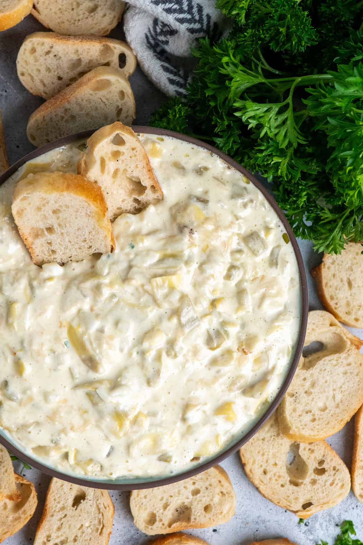 Crock Pot artichoke dip in a bowl surrounded by sliced bageuttes.