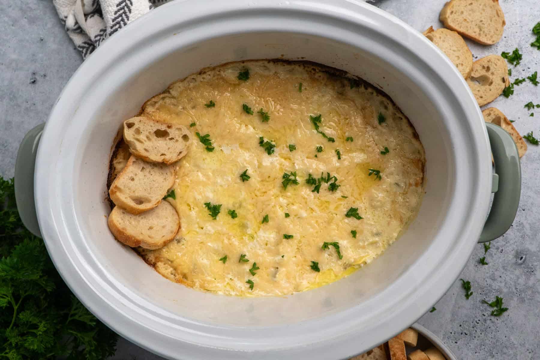 Crock pot artichoke dip garnished with parsley and baguettes.