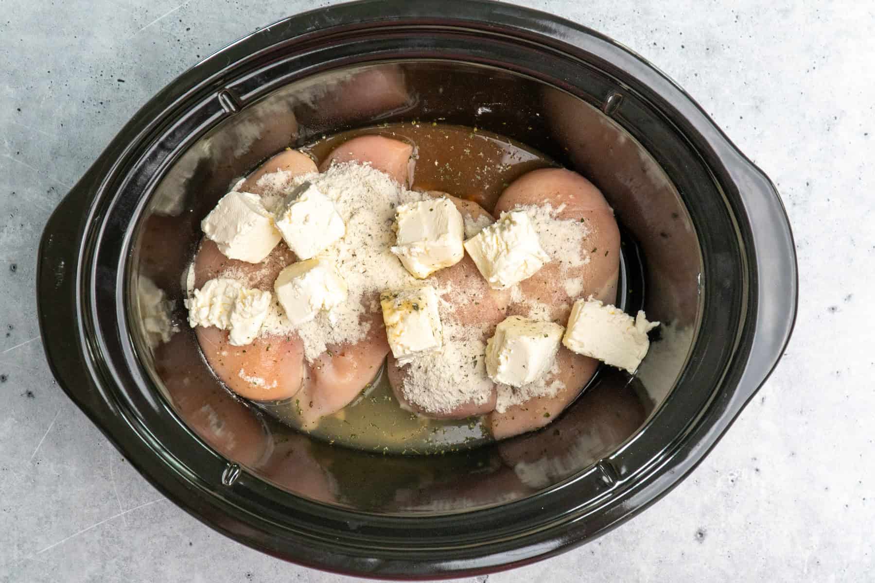 Four raw chicken breasts, ranch seasoning, cream cheese and chicken broth in a slow cooker.