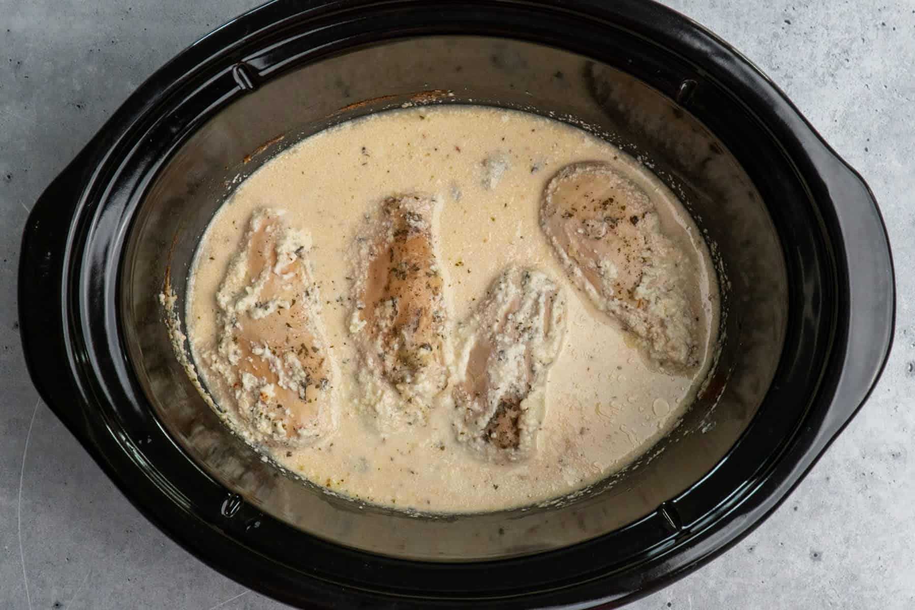 Four cooked chicken breasts, ranch seasoning, cream cheese and chicken broth in a slow cooker.