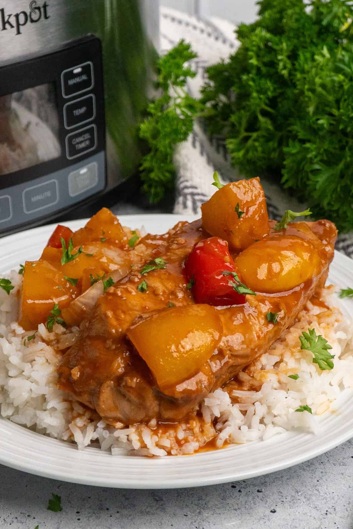 Hawaiian pork chops on a plate of rice with a slow cooker in the background.