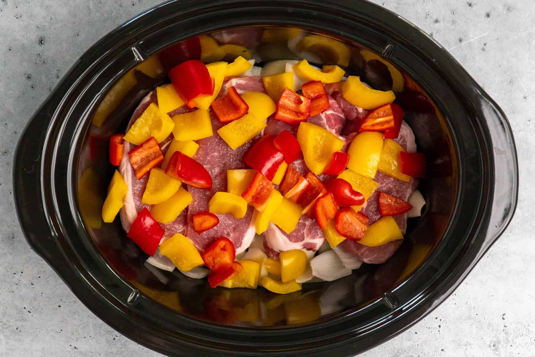 Uncooked pork chops, onions, and bell peppers in a slow cooker.