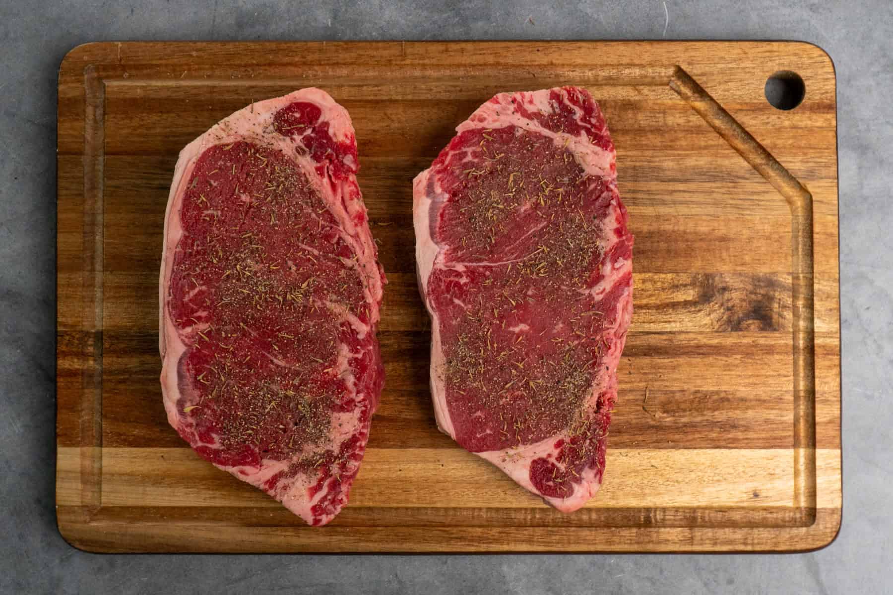 Ribeye steaks on a cutting board and sprinkled with seasoning.