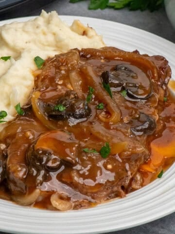 Ribeye steak in a crock pot served up on a plate with mashed potatoes ready to eat.