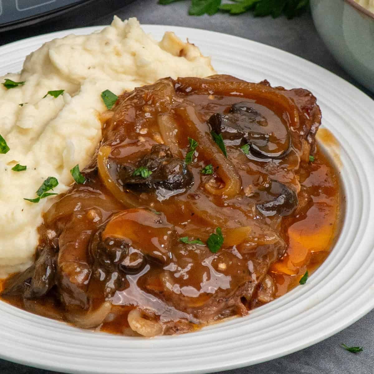 Ribeye steak in a crock pot served up on a plate with mashed potatoes ready to eat.