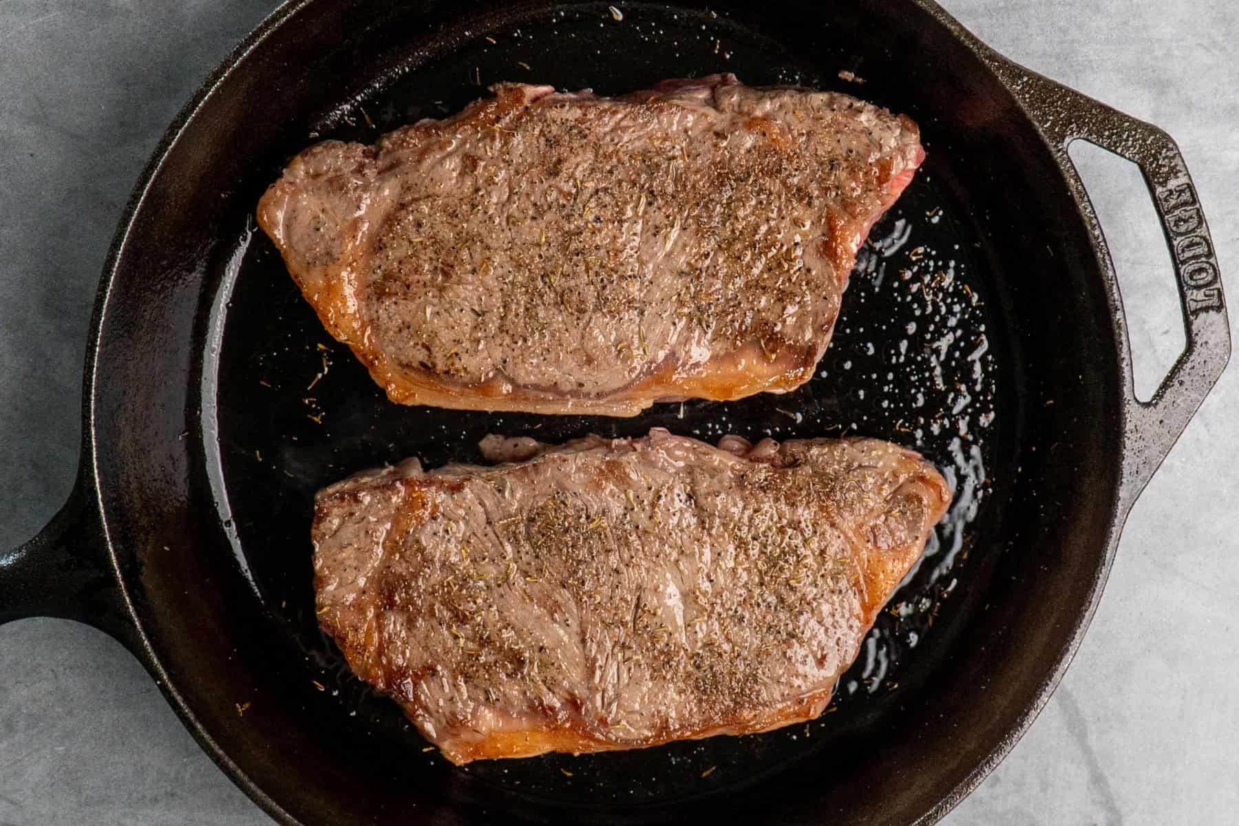 Ribeye steaks in a cast iron skillet that have been seared on both sides.