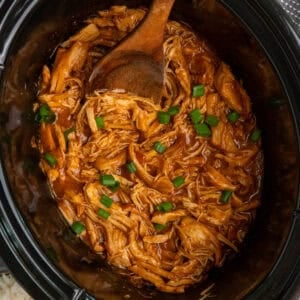 Shredded apricot chicken in a crock pot and garnished with green onions.