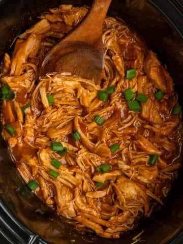 Shredded apricot chicken in a crock pot and garnished with green onions.