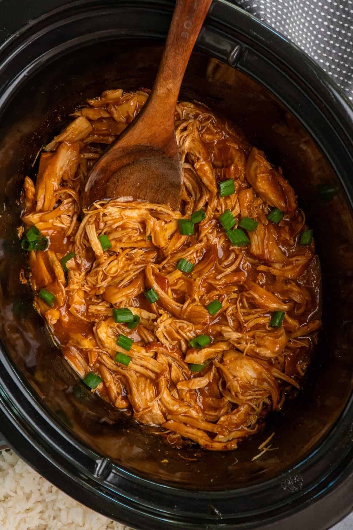 Shredded apricot chicken in a crock pot and garnished with green onions.