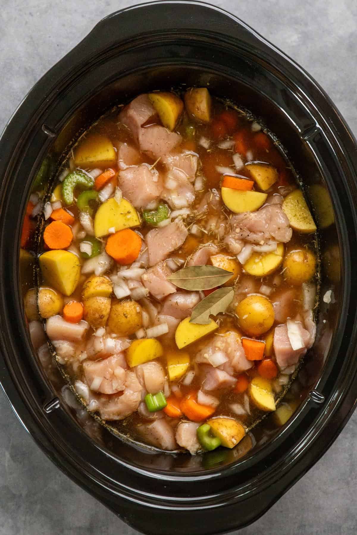 Broth and seasonings added to the chicken and vegetables in the slow cooker.