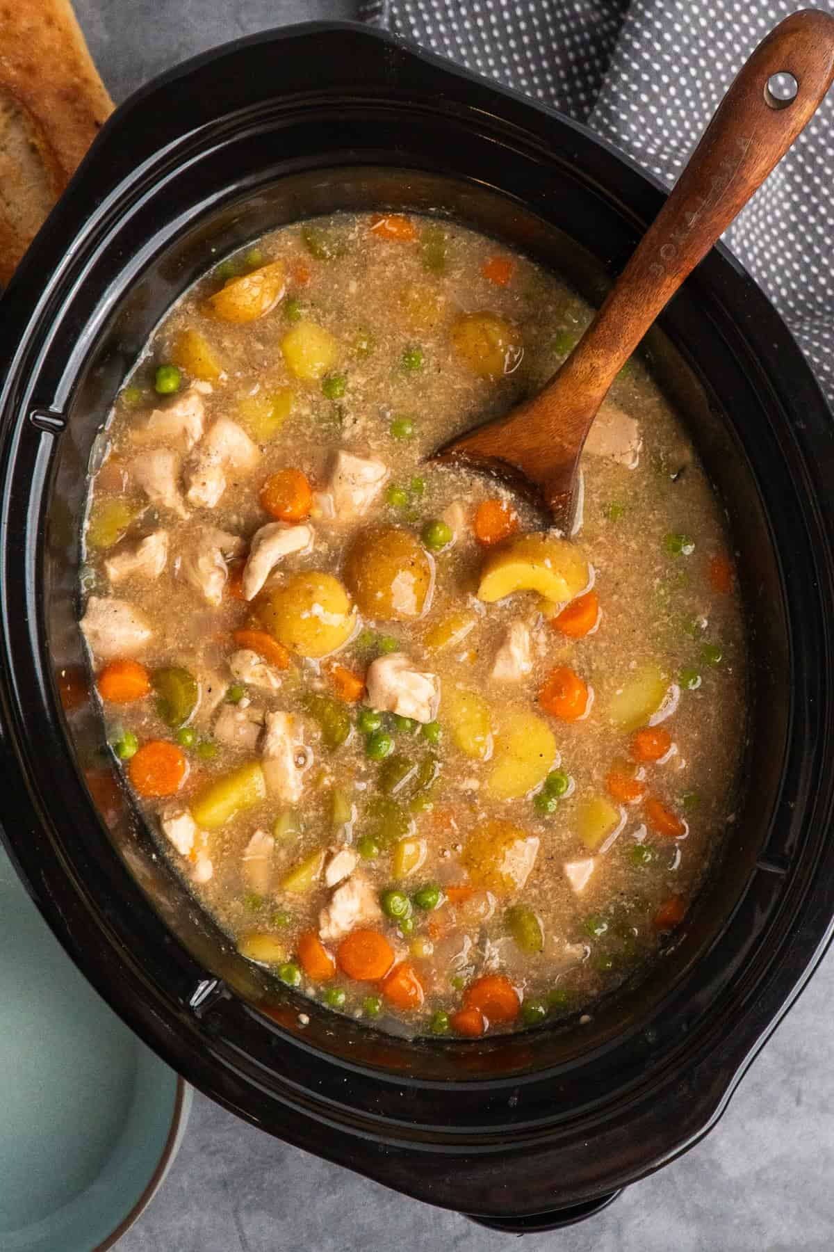 Chicken stew in a slow cooker with a wooden spoon in the stew leaning on the side. 