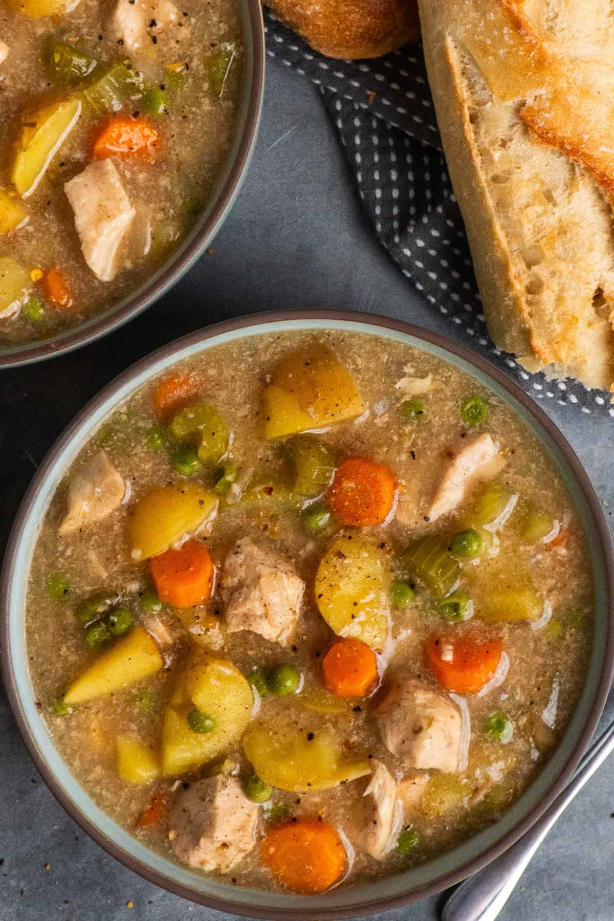 Bowls of chicken stew on a table top with a french bread torn in half next to the bowls.