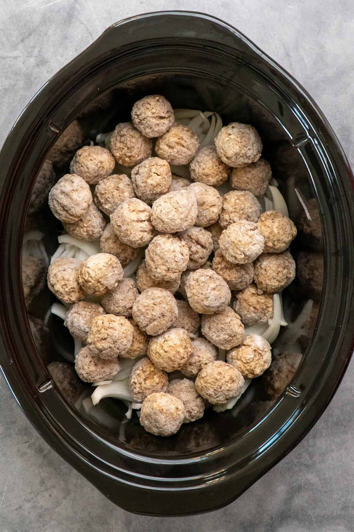 Frozen meatballs on top of sliced onions in a slow cooker.