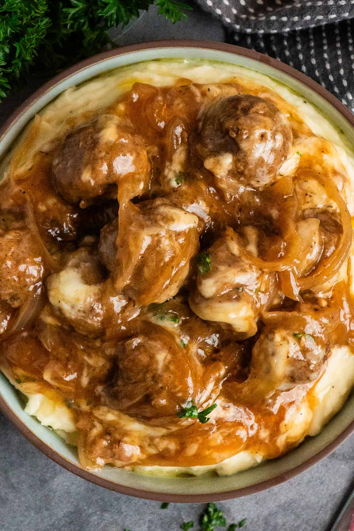 Slow cooker French onion meatballs over a bowl of mashed potatoes.