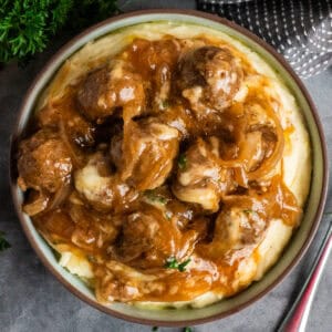 Slow cooker French onion meatballs over a bowl of mashed potatoes.