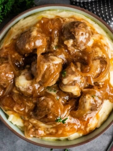 Slow cooker French onion meatballs over a bowl of mashed potatoes.