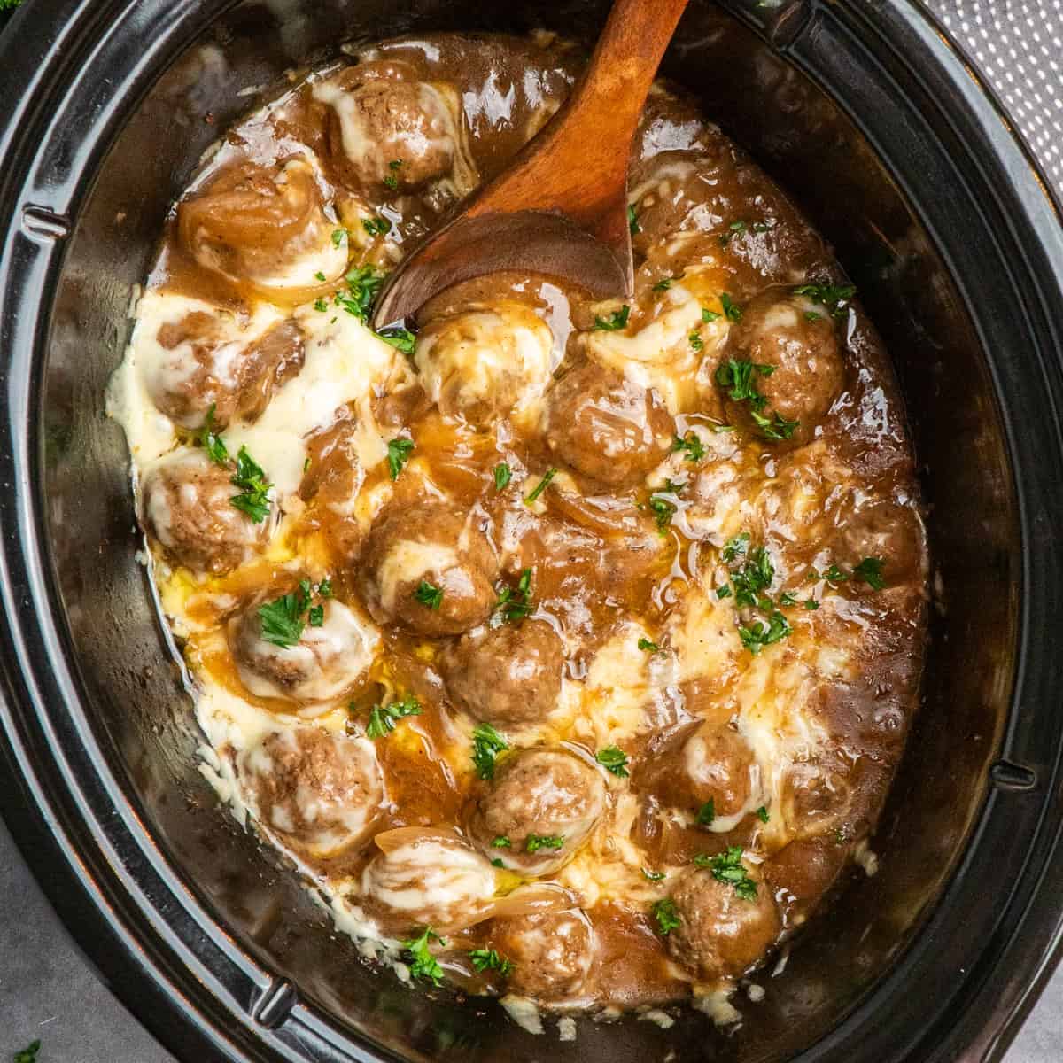 French onion meatballs in a slow cooker with a wooden spoon ready to be served.