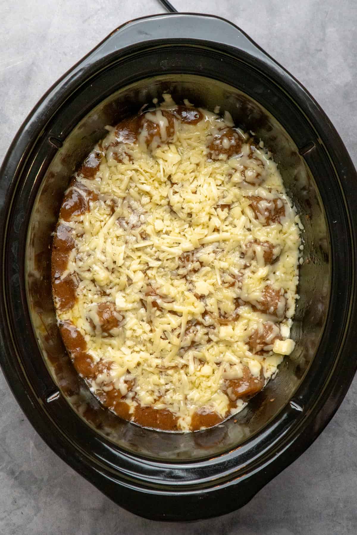 Shredded cheese on top of cooked meatballs.