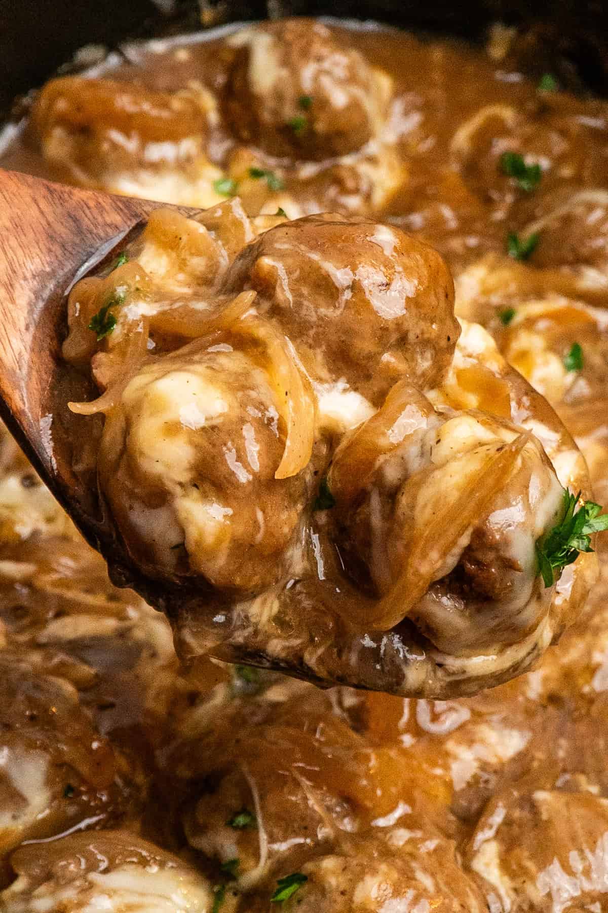 A wooden spoon holding a scoop of french onion meatballs.