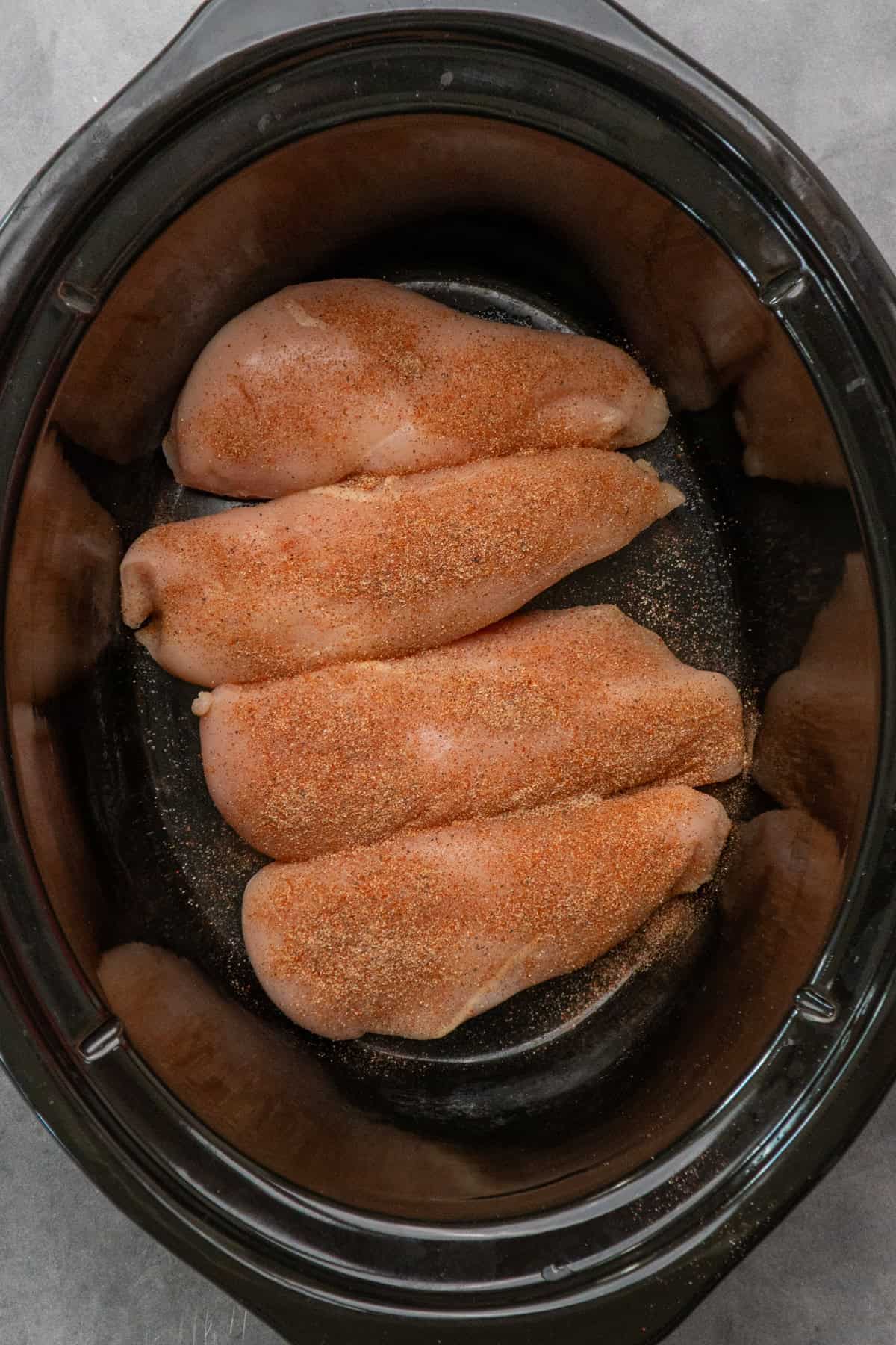 Chicken breasts in a slow cooker sprinkled with seasonings.